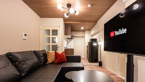 A modern living room with a black leather sofa, a small round table, and a flat-screen TV mounted on the wall. - Bird Land in Shinsaibashi east (Osaka)