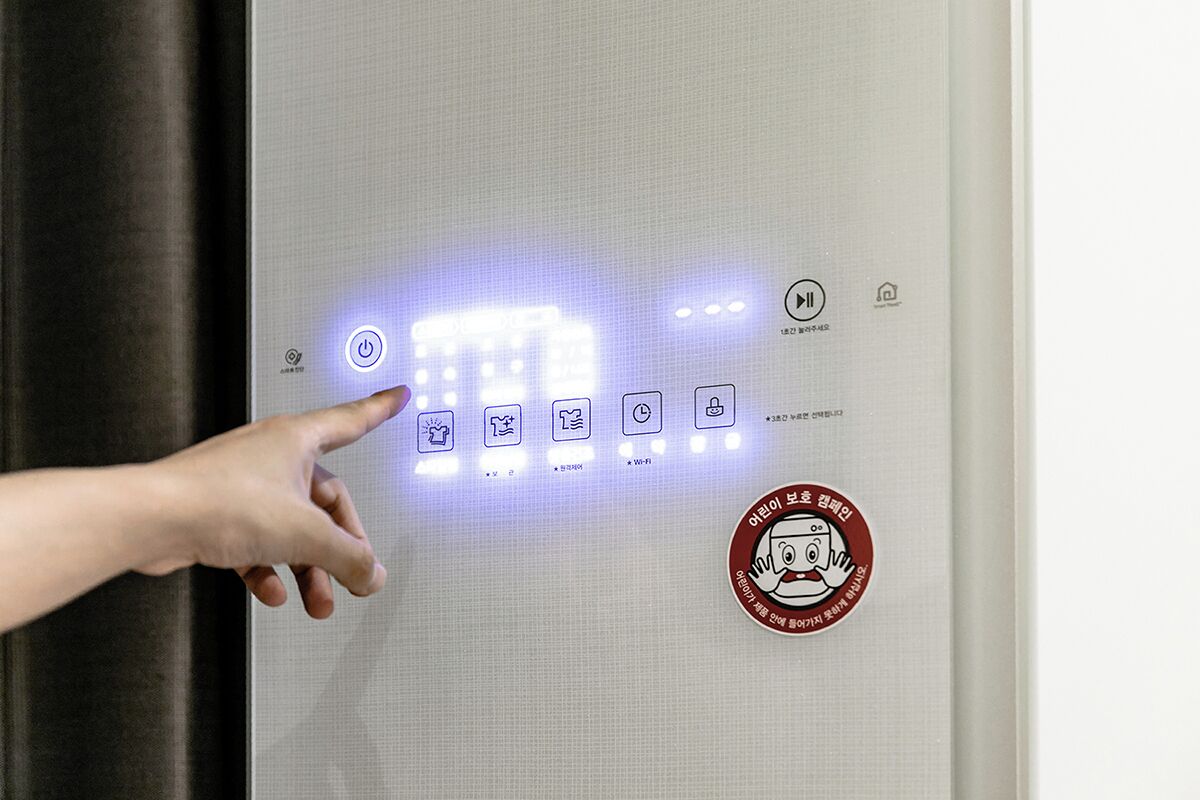 A hand pointing at a control panel with illuminated icons, including a power button and Wi-Fi symbol.
