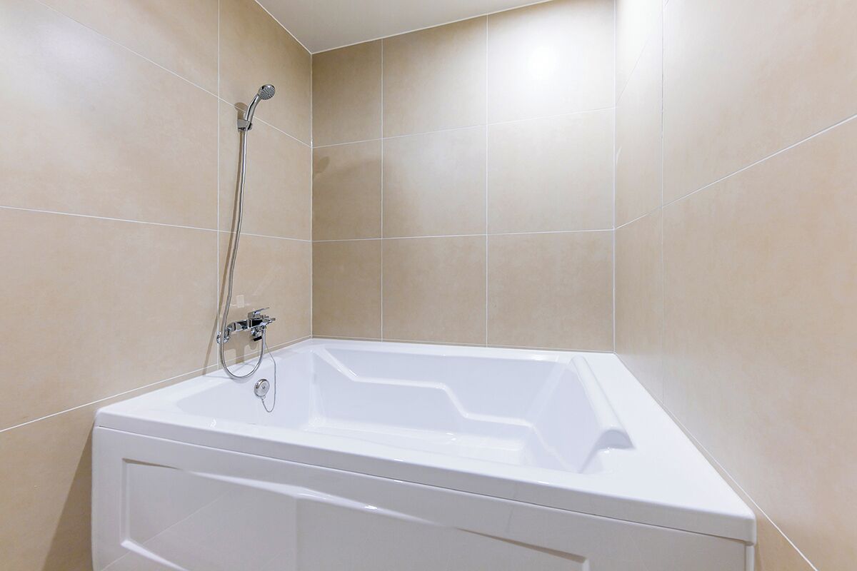 Un baño con una bañera blanca, un cabezal de ducha y paredes de azulejos color beige.