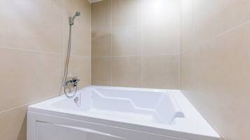 Un baño con una bañera blanca, un cabezal de ducha y paredes de azulejos color beige.