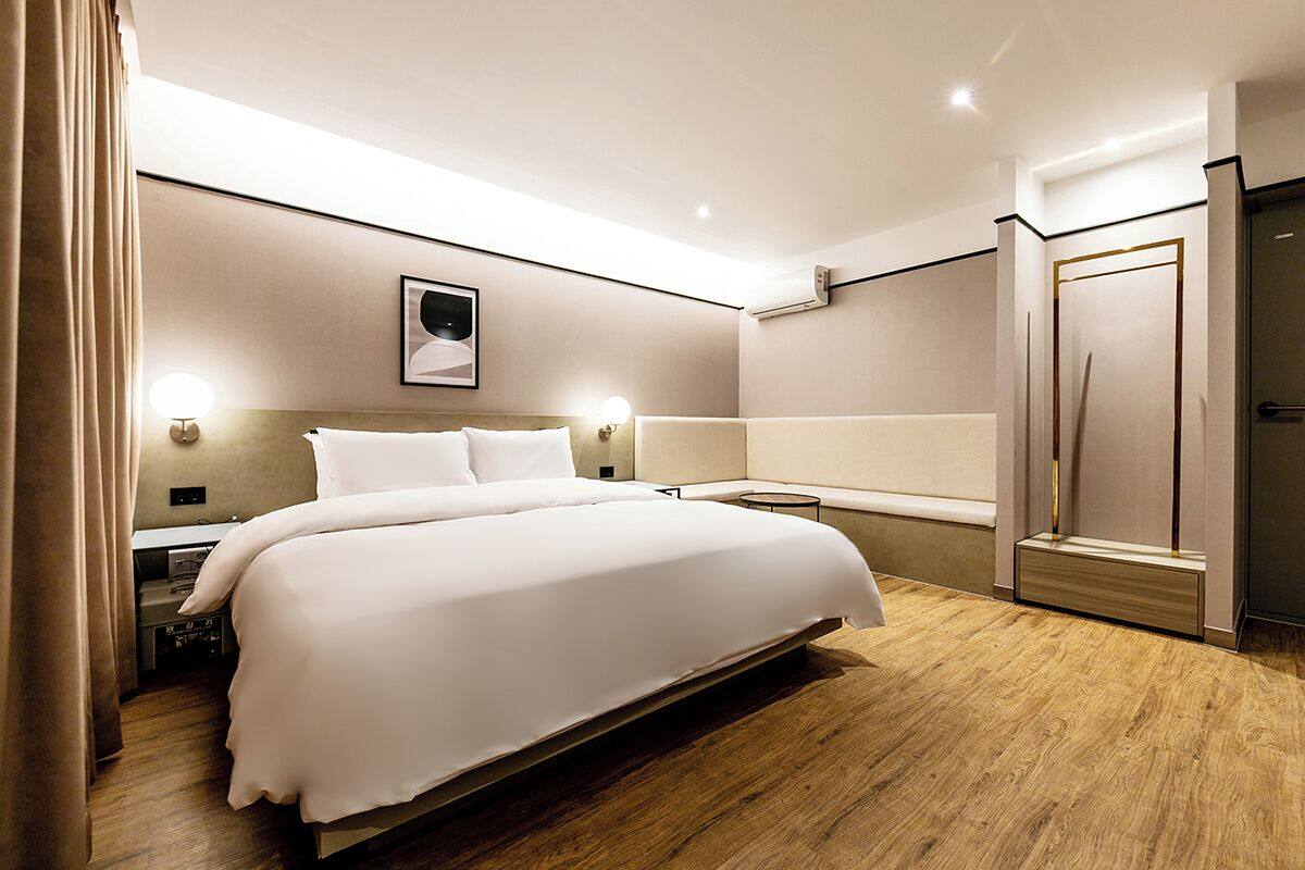 A modern hotel room with a large bed, bedside lamps, a wall-mounted air conditioner, and a wooden floor.