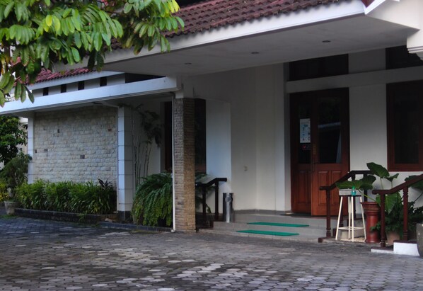 A building with a stone facade, a wooden door, and a green mat leading to the entrance. - Hotel Graha Kinasih Kotabaru (Yogyakarta)