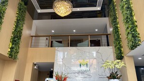 Un comptoir d’accueil moderne, doté d’un plateau en marbre, entouré de plantes et surmonté d’un lustre.