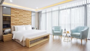 Une chambre d’hôtel moderne avec un grand lit, deux fauteuils, une petite table et un téléviseur posé sur un meuble.