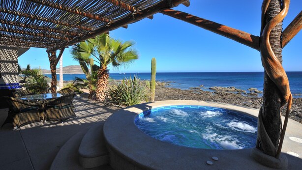 Uma banheira de hidromassagem com vista para o oceano, uma mesa e cadeiras, e uma palmeira.