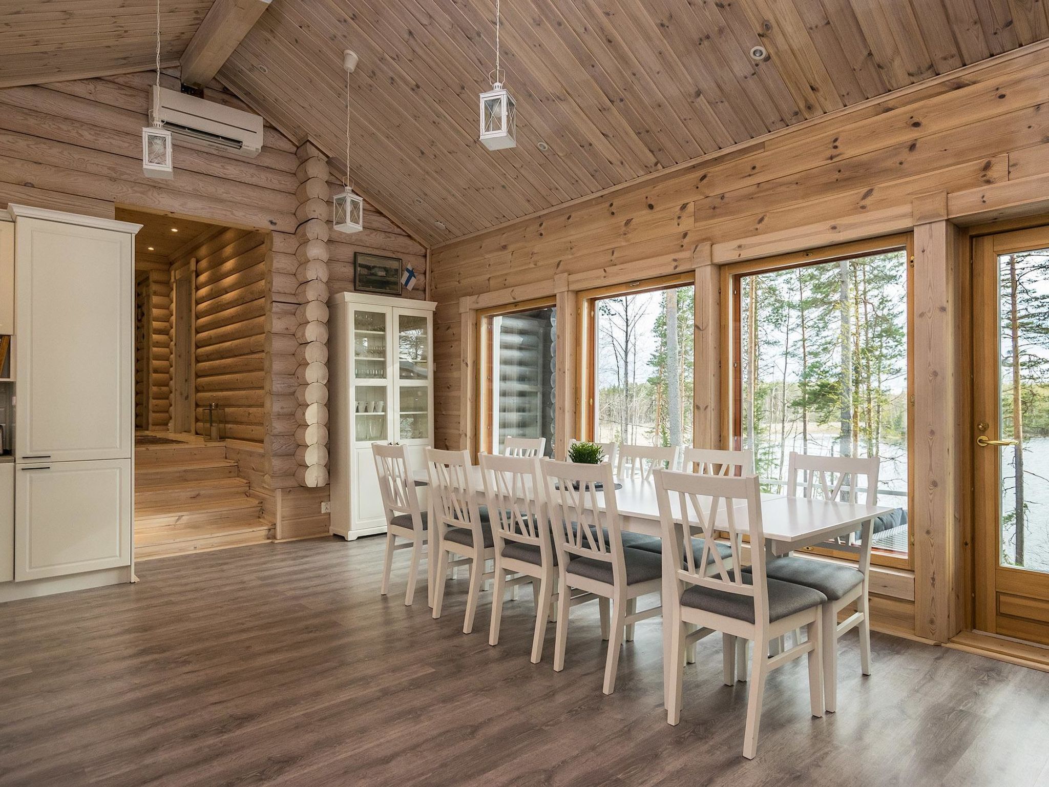 A log cabin interior with a dining area, white cabinetry, and large windows.