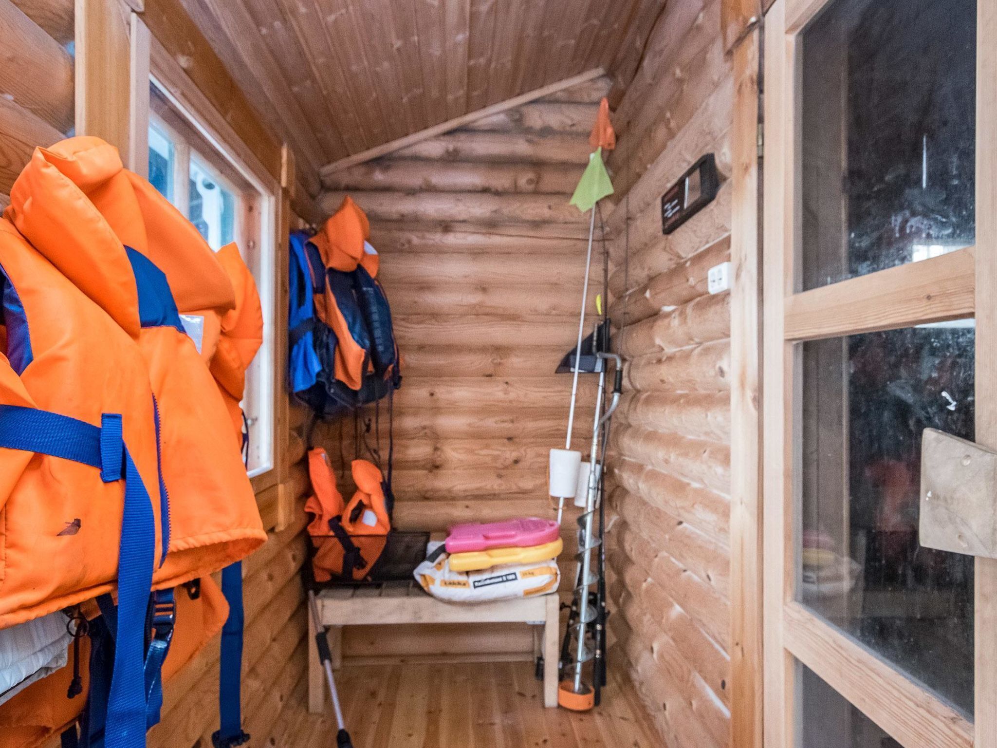 A cabin with wooden walls, a window, and a shelf with life jackets and a fishing rod.
