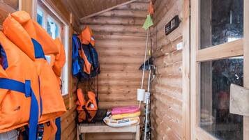 A cabin with wooden walls, a window, and a shelf with life jackets and a fishing rod.