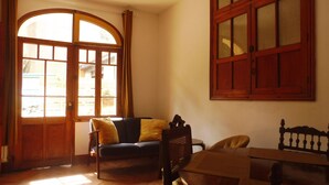 Une pièce avec un plancher en bois, un canapé avec des coussins jaunes, une table en bois et une fenêtre avec un cadre en bois.