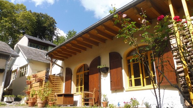 Un chalet traditionnel avec une façade en bois, de nombreuses fenêtres dotées de volets et un escalier en pierre menant à l’entrée.