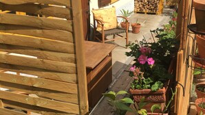 Une terrasse en bois avec un banc et une table, entourée de plantes et de fleurs en pot.