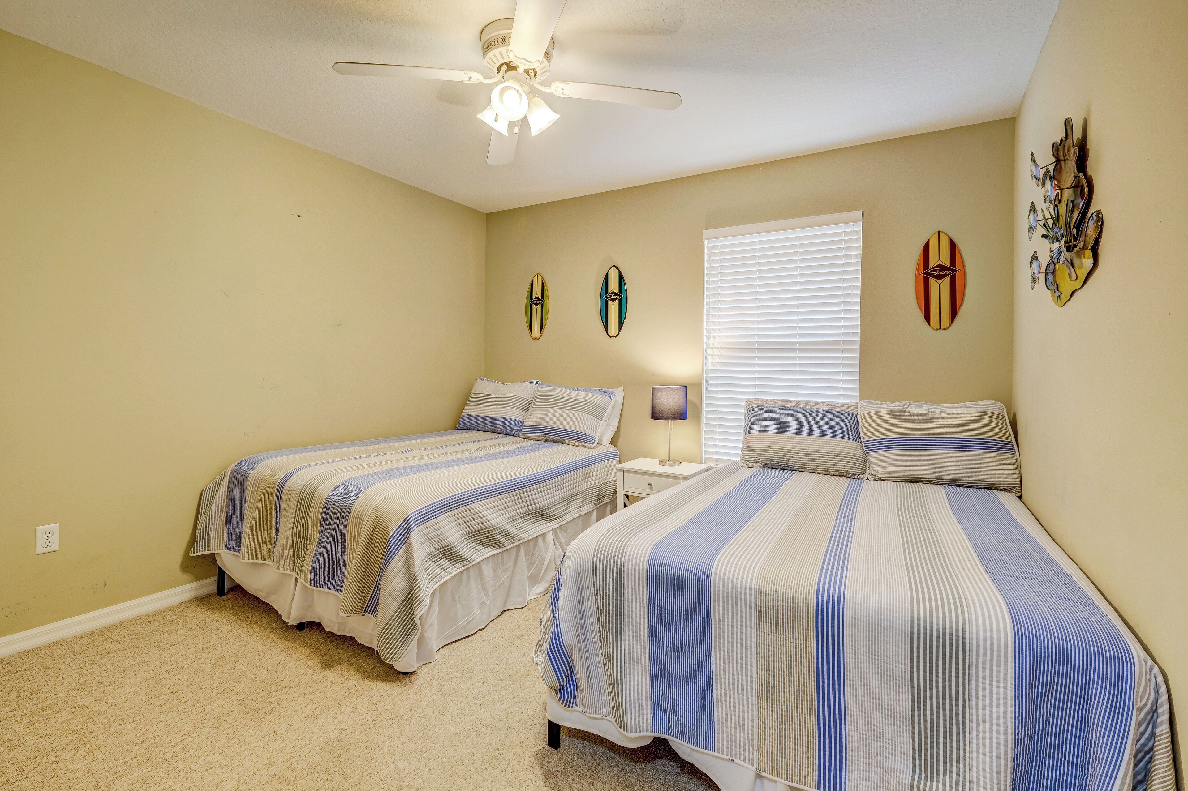 A bedroom with two beds, a ceiling fan, and surfboard decorations on the wall.