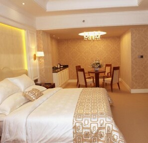 A hotel room with a large bed, a dining table with chairs, and a chandelier.