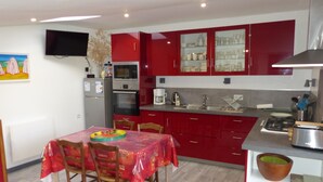 A kitchen with red cabinets, a dining table with chairs, a microwave, a coffee maker, and a TV mounted on the wall. - Gîte 4 persons; Autour d'un Puits (Marsilly)