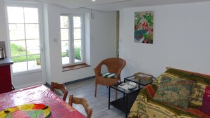 A bright room with a dining table, a wicker chair, a sofa, and a painting on the wall. - Gîte 4 persons; Autour d'un Puits (Marsilly)