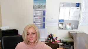 Una mujer sentada en un escritorio con una computadora, rodeada de material de oficina y documentos.