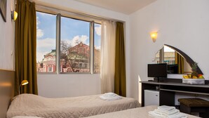 Habitación de hotel con dos camas, un escritorio con ordenador, un espejo y una ventana con cortinas.