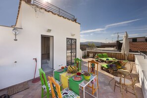 Een terras op het dak met buitenmeubilair, een tafel met fruit en kommen, en een uitzicht op de stadslijn.
