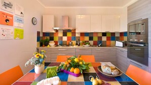 Una cocina moderna con un salpicadero de azulejos coloridos, electrodomésticos de acero inoxidable y una zona de comedor con mantel a cuadros y varios alimentos.