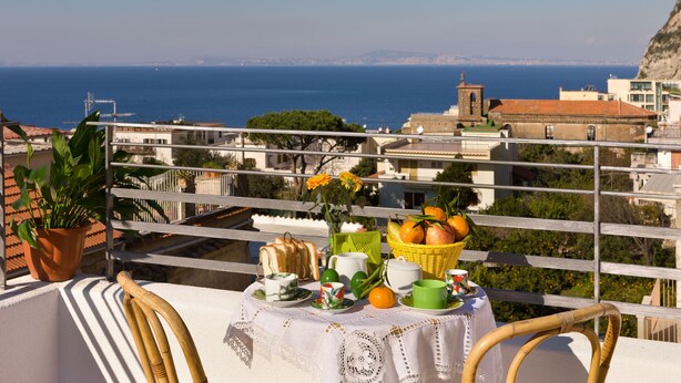 Un balcón con una mesa dispuesta para el desayuno, con vista a una ciudad costera.