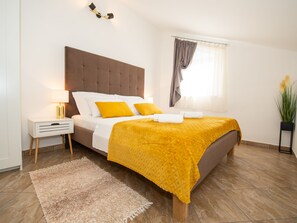 A bedroom with a bed, a bedside table, a lamp, a window with curtains, and a plant. - Holiday Home near Trogir (Kastela)