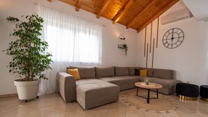 A modern living room with a sectional sofa, a potted plant, a round coffee table, and a wall clock. - Holiday Home near Trogir (Kastela)