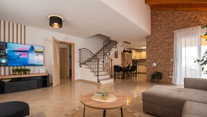 A modern living room with a TV, sofa, coffee table, and a staircase leading to a dining area. - Holiday Home near Trogir (Kastela)