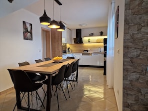 A modern kitchen with white cabinets, a wooden countertop, and a stone wall. There is a dining area with a wooden table and black chairs. - Holiday Home near Trogir (Kastela)