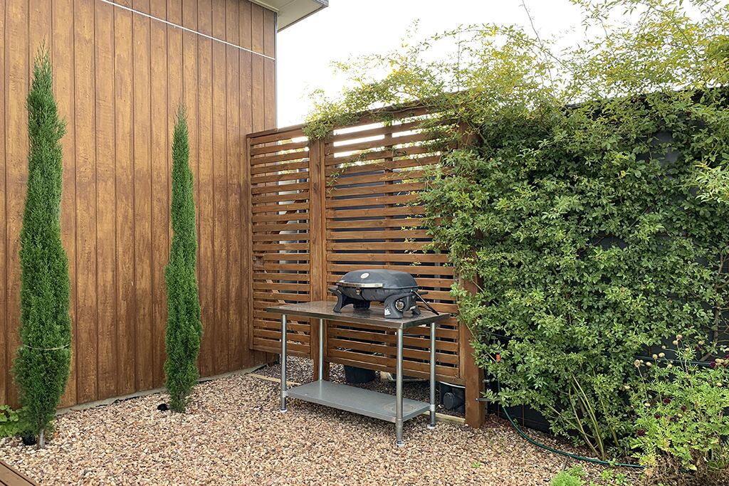 Un patio con una parrilla, cerca de madera y seto.