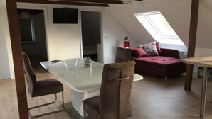 Una habitación moderna estilo loft con una mesa de comedor, dos sillas, un sofá y una pequeña mesa con un farol rojo.