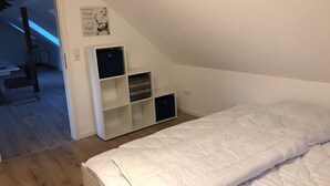 Un dormitorio con una cama blanca, un armario blanco y un escritorio pequeño.