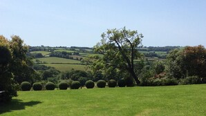 A stone pathway leading to a grassy area with a view of rolling hills and a large tree in the distance. - Grade 1 listed Medieval Hall House near the Devon and Cornwall border (Leat)