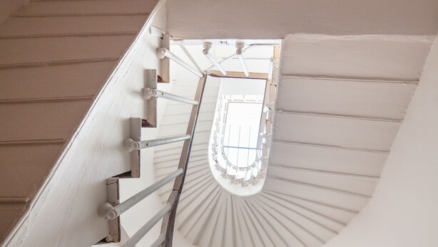 A spiral staircase with white railings and a view of a room at the top.