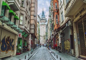 A cobblestone street lined with historic buildings, a prominent church spire, and closed shops. - Maravilloso Hotel Galata (Istanbul)