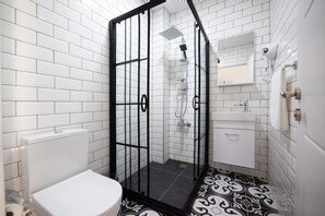 A bathroom with white tiled walls, a black and white patterned floor, a white toilet, a shower with a black frame, and a white sink with a mirror above it. - Maravilloso Hotel Galata (Istanbul)