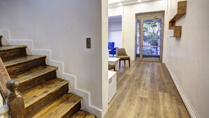 A staircase with wooden steps leading to a room with a desk and chair, a door with a glass panel, and a view of the outdoors.