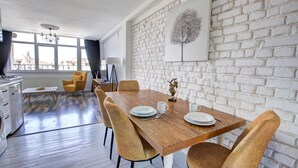 A dining area with a wooden table, four chairs, and a white brick wall with a tree artwork.