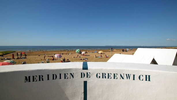 En strand med en skylt som visar texten ”MERIDIENEN I GREENWICH”.
