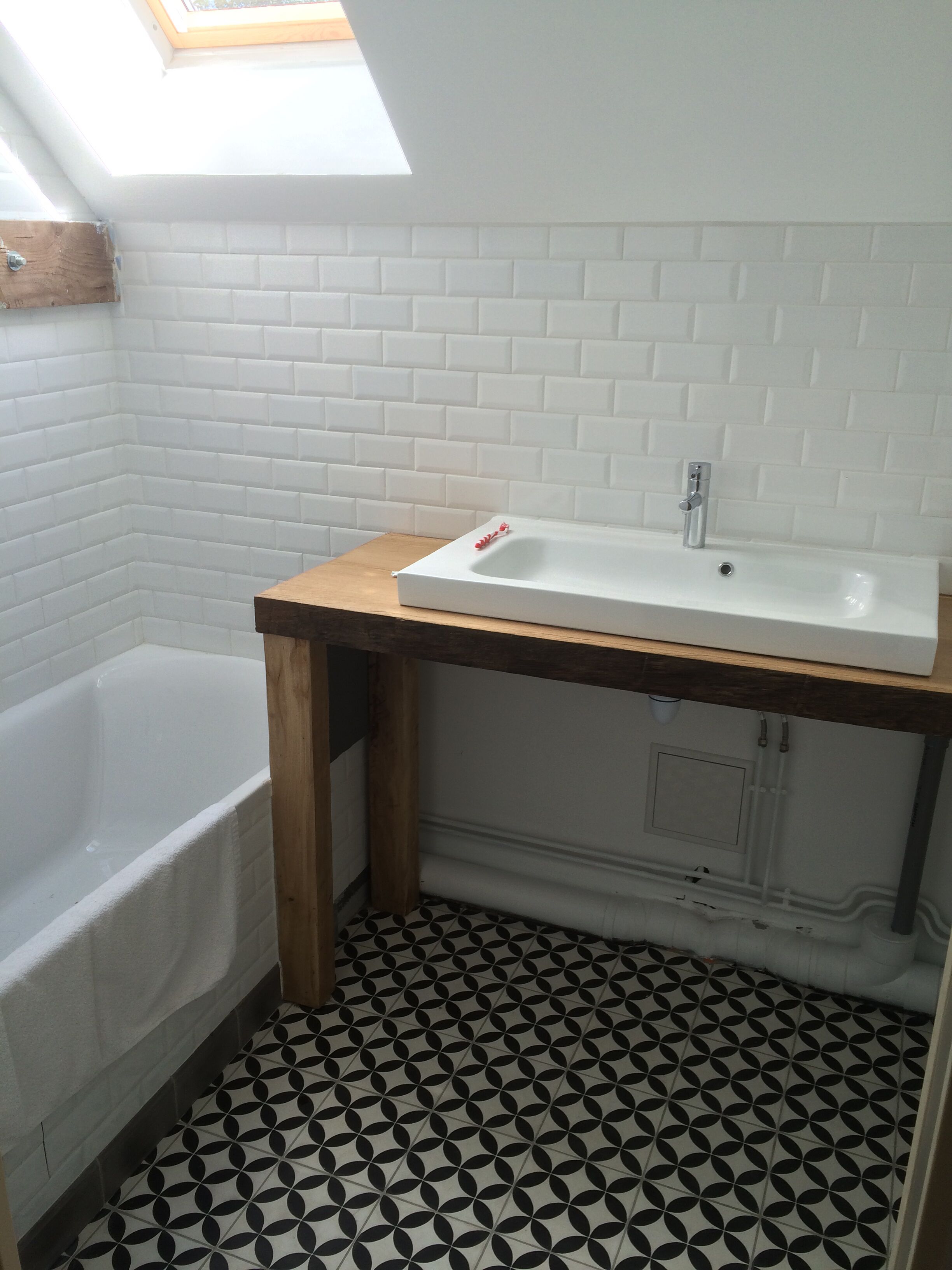 Une salle de bain avec une baignoire blanche, un meuble-lavabo en bois et un carrelage noir et blanc à motifs.