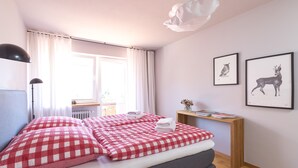 Quarto com colcha xadrez, mesa de cabeceira com livros e quadros de animais na parede.