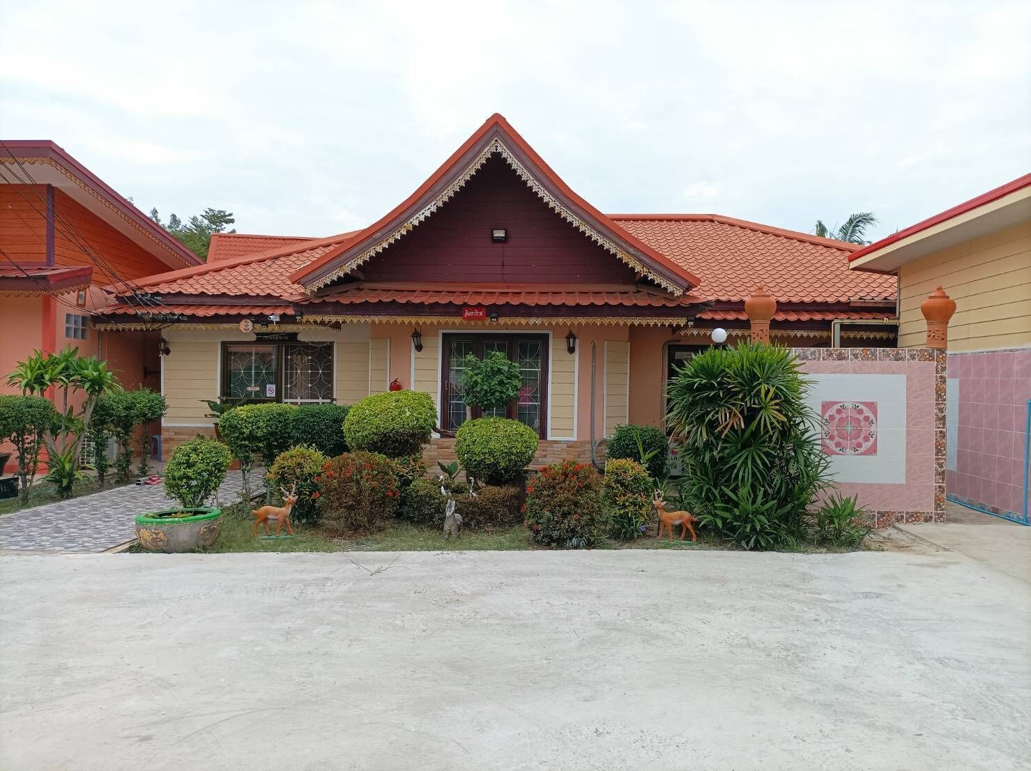 A traditional house with a red tiled roof, a central entrance with a decorative arch, and a well-maintained garden with various plants and a small deer statue.