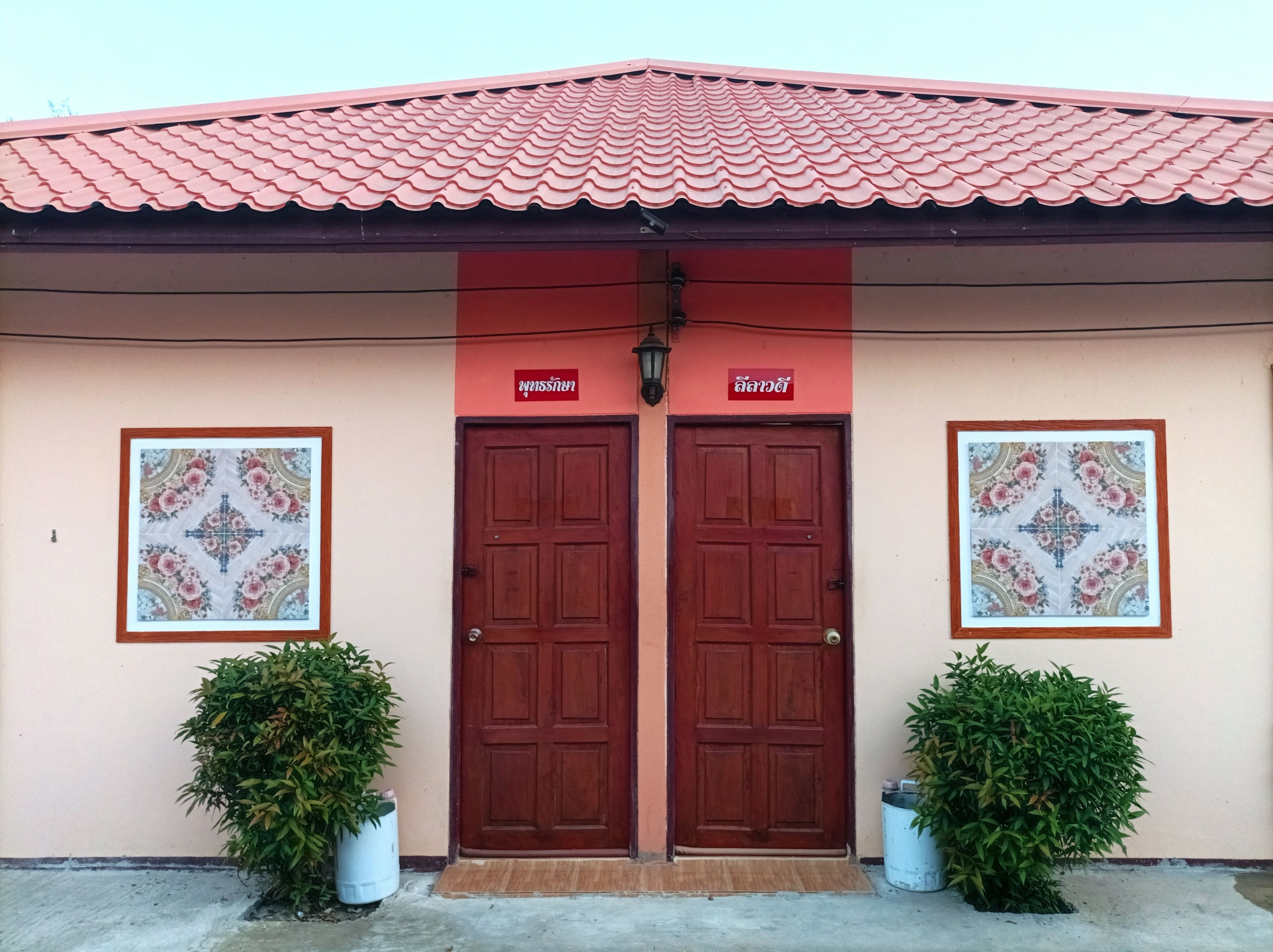 A building with a red tiled roof, two wooden doors, and two framed floral patterns on the walls.