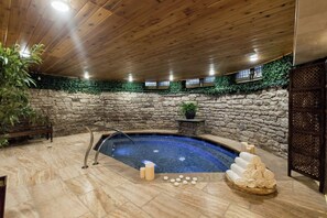 Un área de spa con jacuzzi, paredes de piedra, techo de madera y una banca.