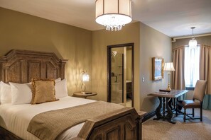 A hotel room with a large bed, a wooden headboard, a desk with a chair, a chandelier, and a mirror on the wall. - The Detroit Club (Detroit)