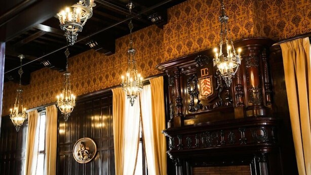 A room with dark wooden paneling, ornate chandeliers, and a large, decorative fireplace.