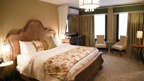 A hotel room with a large bed, a wooden headboard, a desk, two armchairs, and a chandelier.