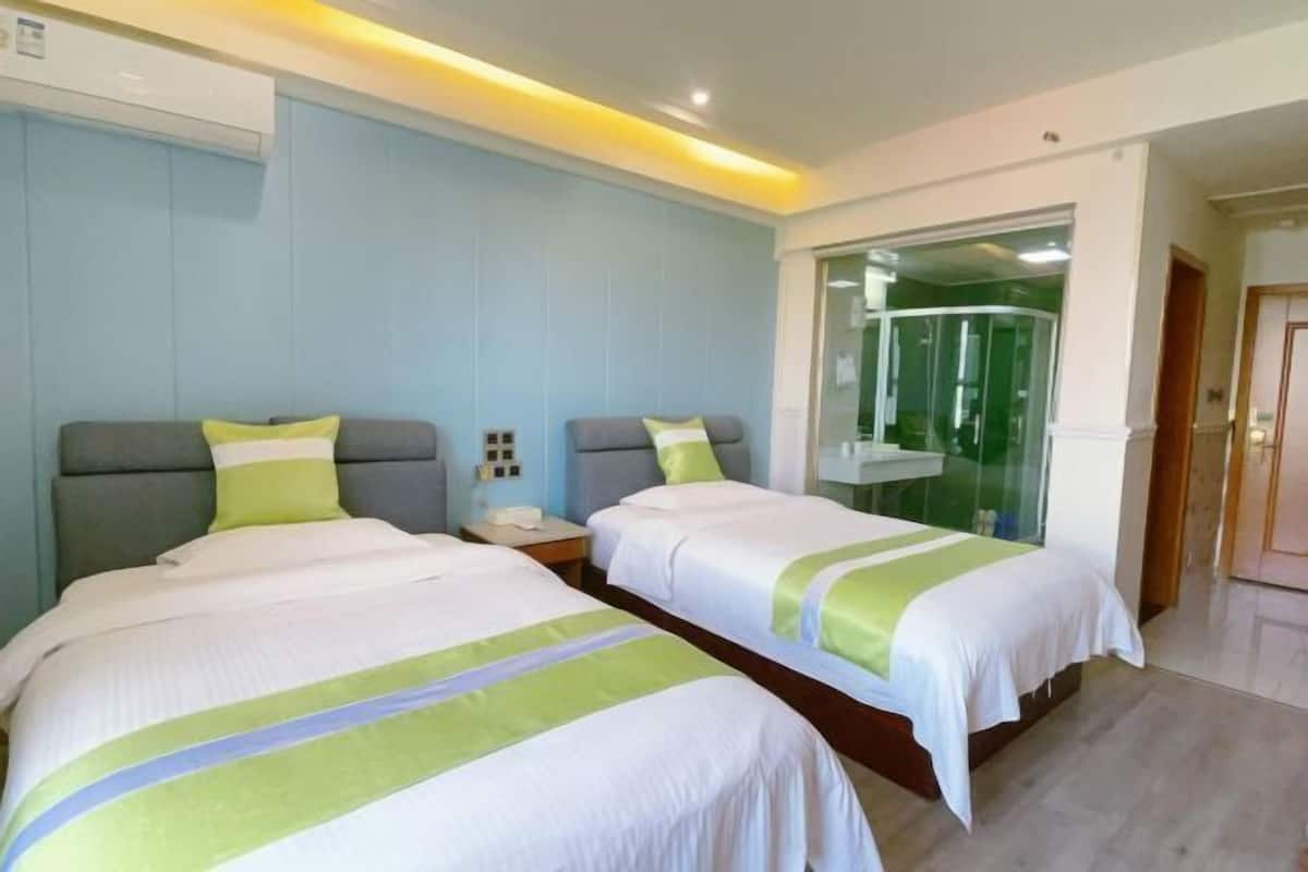 A hotel room with two beds, a glass shower enclosure, and a wooden floor.