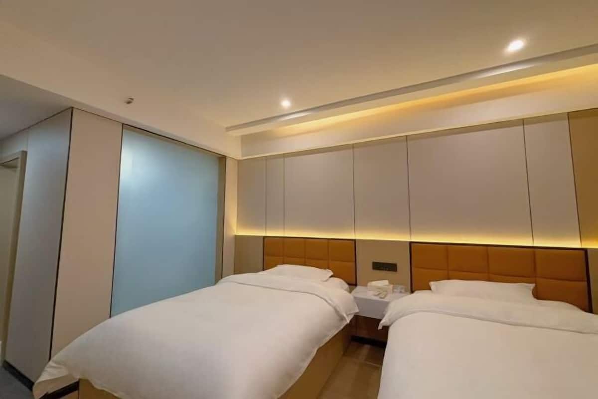 A hotel room with two beds, a bedside table, and a wardrobe.
