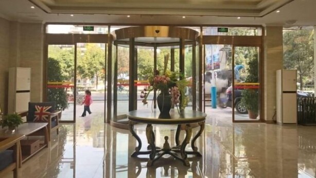 A hotel lobby with a glass door entrance, a round table with a vase of flowers, and a flag on the wall. - GreenTree Inn (Lezhi County Government Branch) (Ziyang)