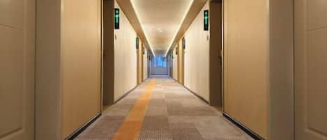 A long, narrow hotel corridor with doors on both sides, carpeted floor, and overhead lighting.